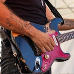 Close-up of a guitarist playing an electric guitar at an outdoor rock concert.