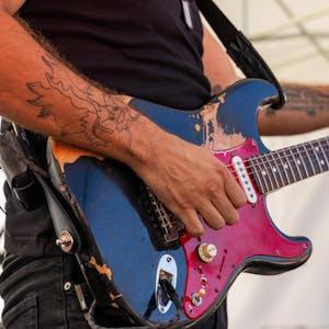 Close-up of a guitarist playing an electric guitar at an outdoor rock concert.